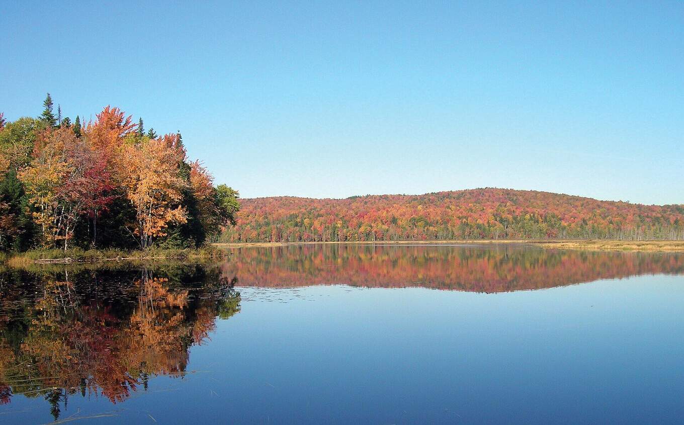 A still lake reflecting a hillside of autumn foliage